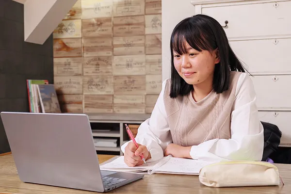 ノートに書き込みながらオンラインレッスンを受ける女子生徒