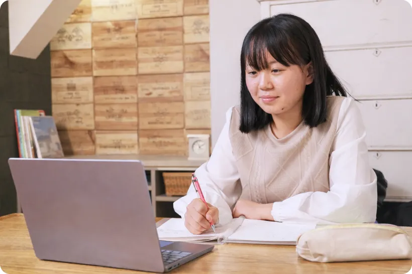 ノートに書き込みながらノートパソコンで学習する子供